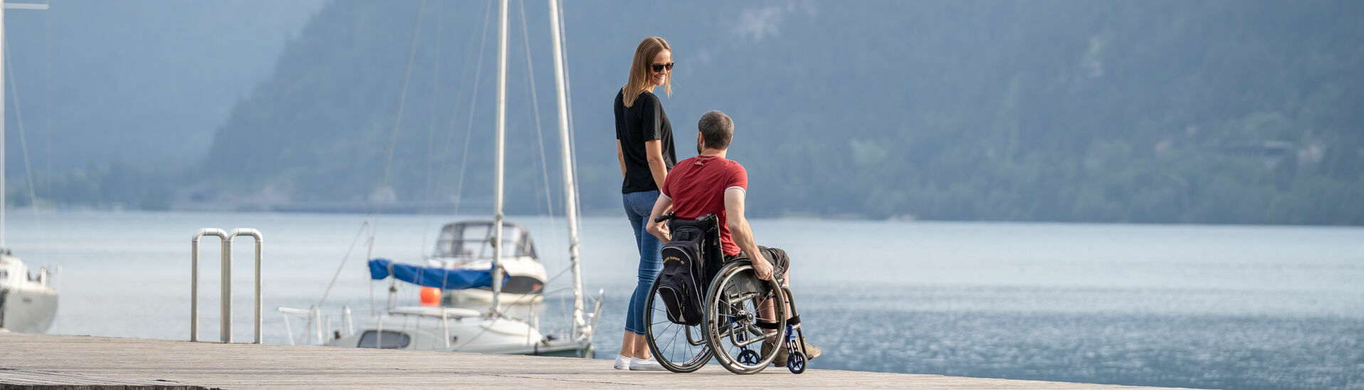 Barrierefrei am Achensee Ein Mann im Rollstuhl und eine Frau befinden sich auf dem Steg bei der Seeuferpromenade in Pertisau im Sommer. }