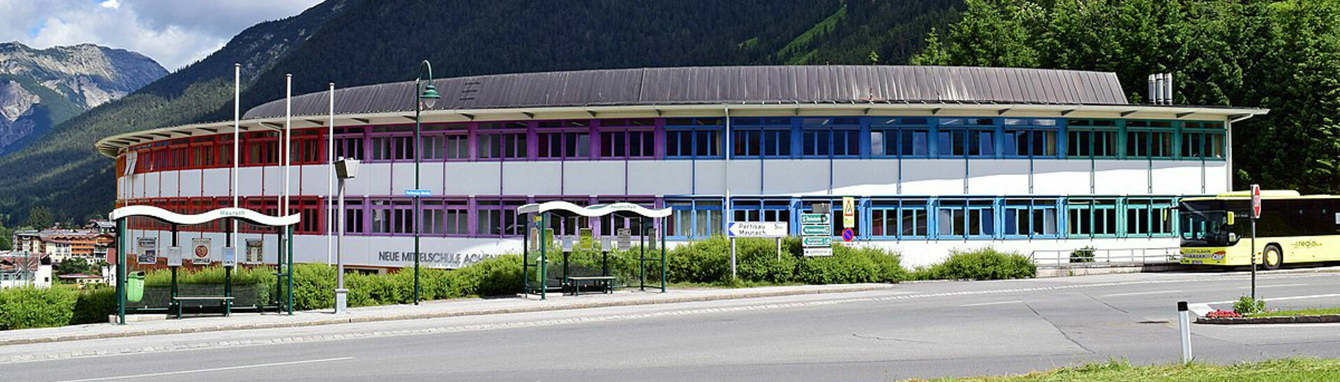 Das farbenfrohe Gebäude der Hauptschule Achensee in Maurach mit der Rotspitze im Hintergrund.}