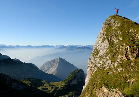 Eine Person steht am Gipfel des Hochiss im Rofangebirge, im Hintergrund ist eine unbeschreibliche Berglandschaft zu sehen.