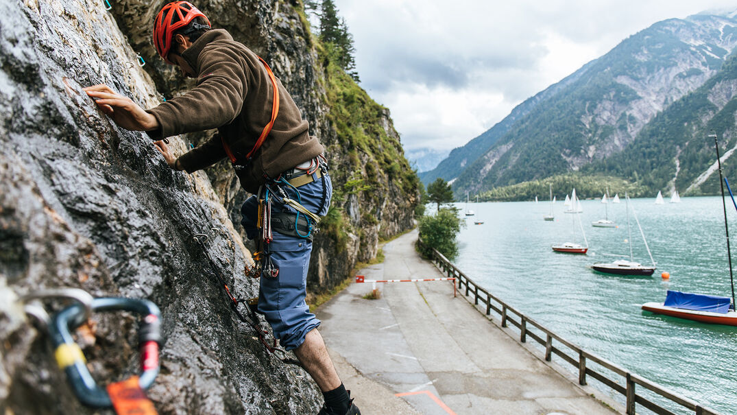 Ein Mann der gerade die Kletterwand am Achenseehof neben dem schönem Achensee besteigt.