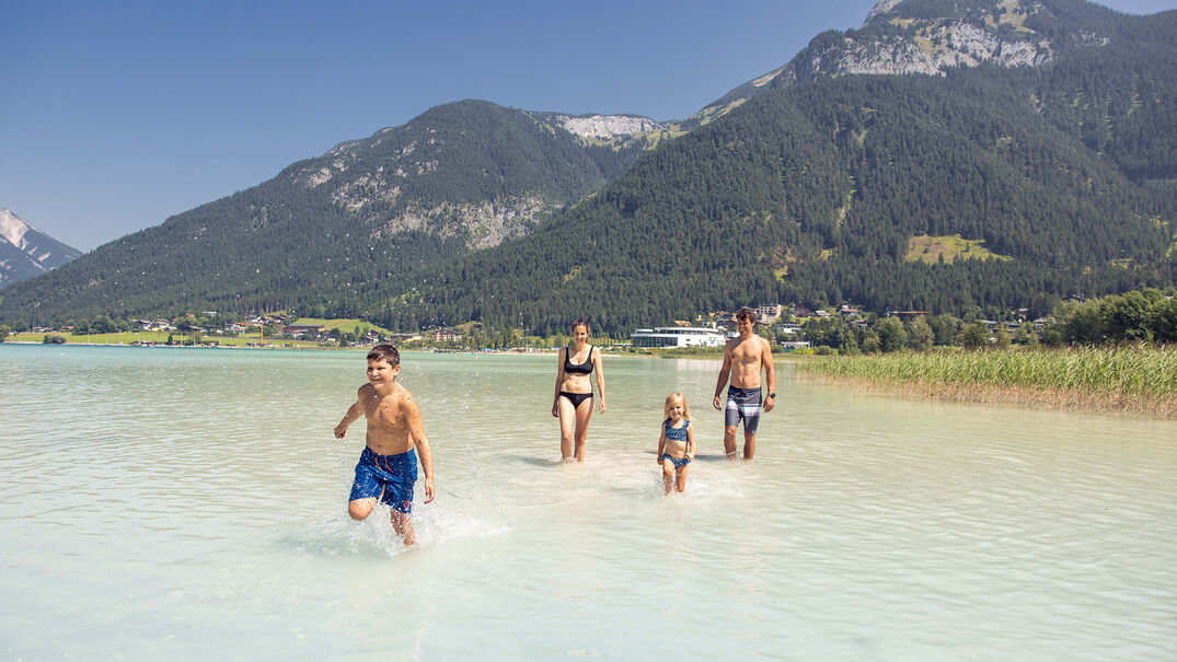 Eine Familie genießt das schöne Wetter und badet im türkisblauen Achensee in Maurach.