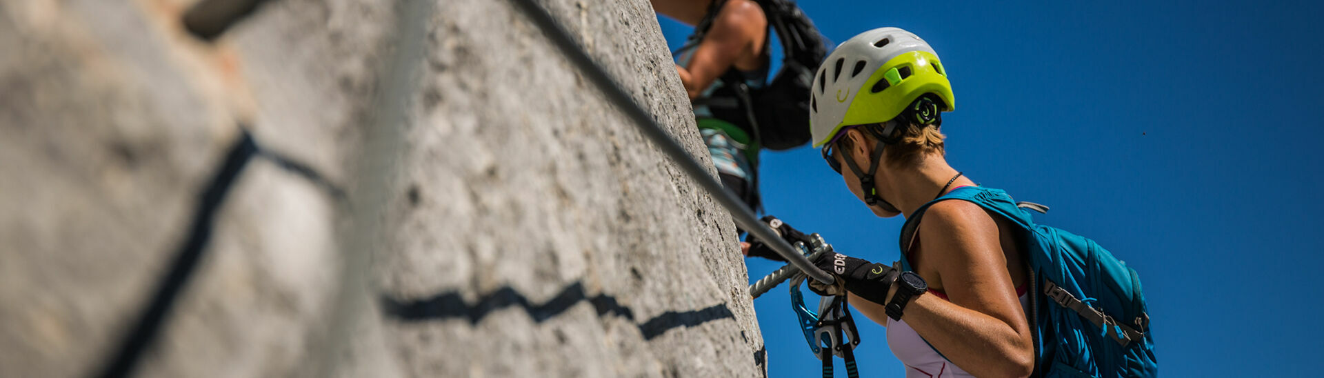 Zwei Frauen klettern an einem im Rofangebirge liegenden Klettersteig bei tollem Wetter und atemberaubendem Ausblick.}