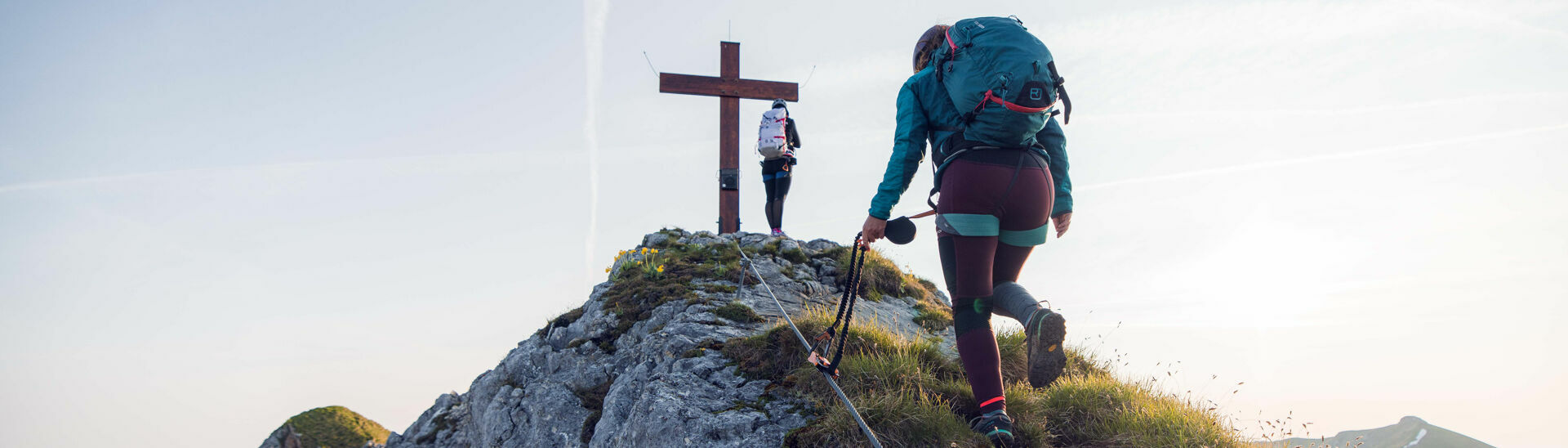 Klettersteig Rosskopf Zwei Frauen kommen gerade am Gipfelkreuz vom Rosskopf an bei schönem Wetter.}