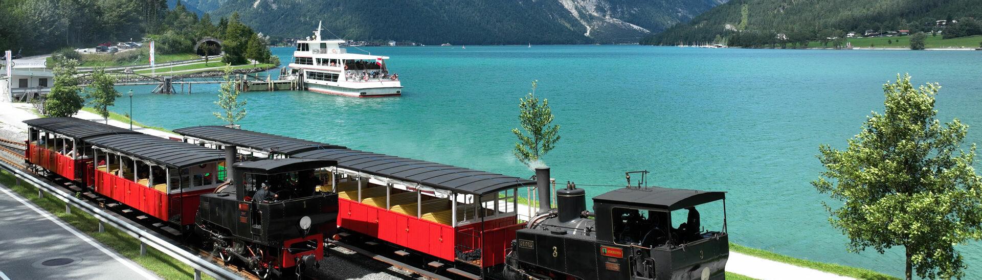 Bahn und Schiff am Achensee Die Luftaufnahme zeigt ein Schiff der Achenseeschifffahrt sowie die Achenseebahn an der Anlegestelle Seespitz im Sommer.}
