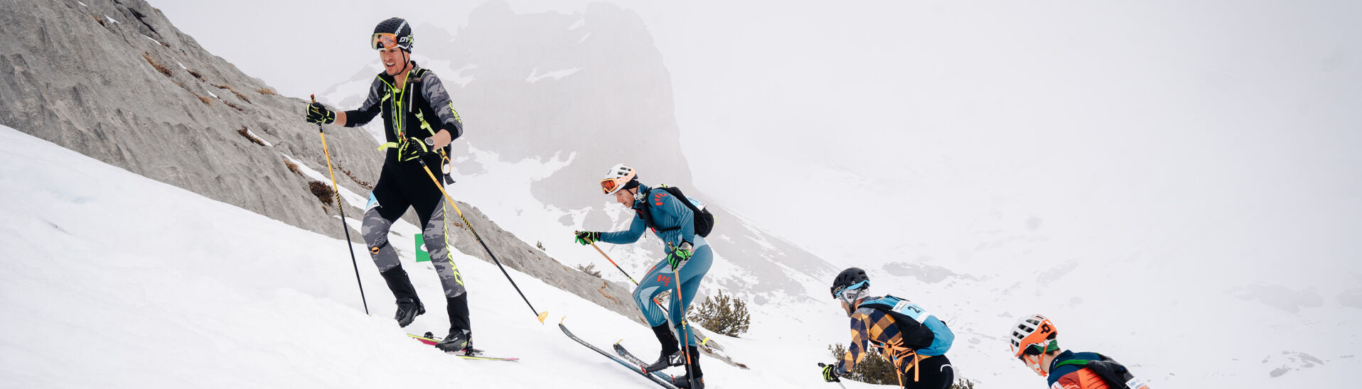 Achensee Xtreme Individual Vier Skifahrer erklimmen einen schneebedeckten Hang im Rofangebirge. Sie tragen technische Ski-Ausrüstung und Skischuhe. Die Umgebung ist gebirgig und in Wolken gehüllt, was die Sicht einschränkt. Alle Sportler sind konzentriert und in Bewegung, während sie den anspruchsvollen Aufstieg bewältigen.}