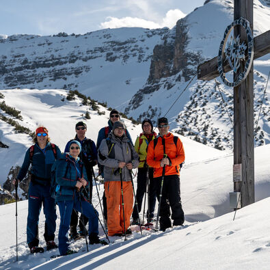A group of snowshoe hikers reach the cross at the Plumssattel and enjoy their summit happiness.