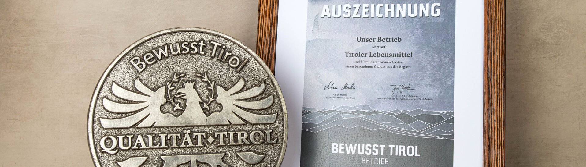 Bewusst Tirol Auszeichnung Ein silbernes Qualitätssiegel mit dem Schriftzug "Bewusst Tirol". Daneben ein gerahmtes Zertifikat mit der Aufschrift "2024 AUSZEICHNUNG" und Informationen über die Unterstützung regionaler Lebensmittel.}