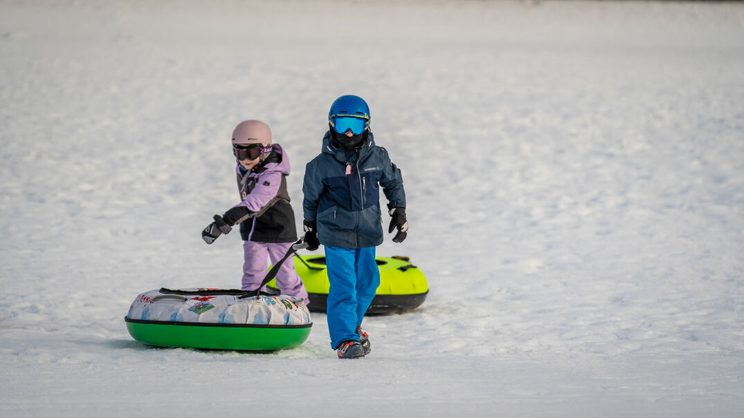 Snowtubing bei den Planberg- & Wiesenliften Zwei Kinder ziehen ihre Snowtubes hinter sich, nachdem sie die eigens dafür ausgewiesene Piste der Planberg- und Wiesenlifte in Pertisau hinuntergerutscht sind.