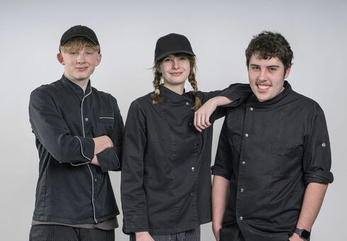 Zwei auszubildende Köche und eine Konditorin posieren vor einer weißen Wand.