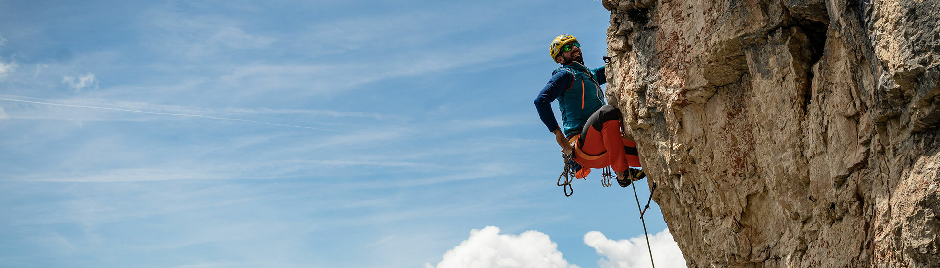 Ein Kletterer der sich gerade neu sichern möchte vor einem schönen blauen Himmel.}