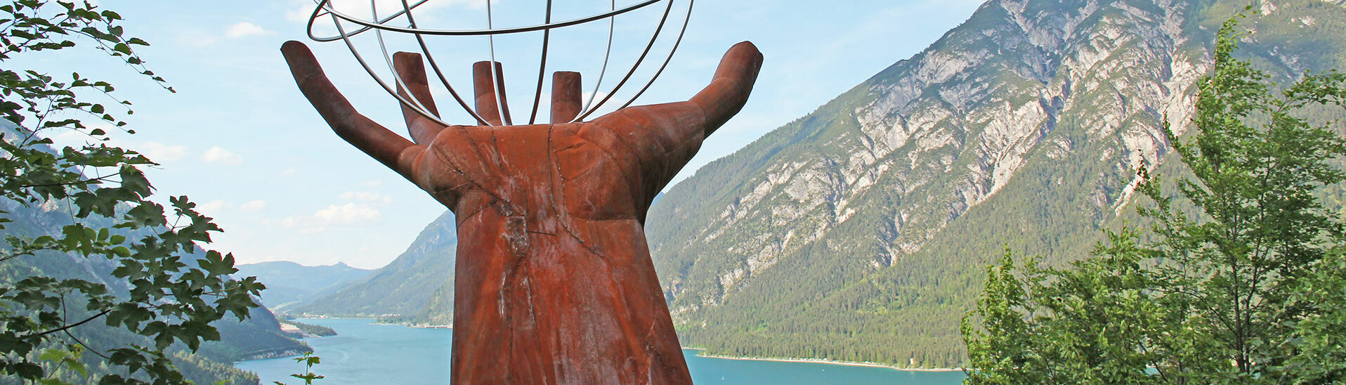 Der Besinnungsweg in Pertisau am Achensee Eine Skulptur einer Hand die einen eisernen durchsichtigen Planeten auf dem Besinnungsweg am in Pertisau hält.}