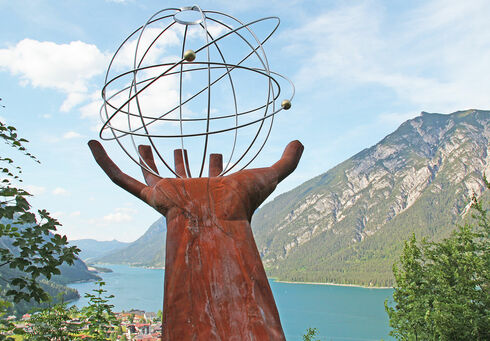 Eine Skulptur einer Hand die einen eisernen durchsichtigen Planeten auf dem Besinnungsweg am in Pertisau hält.
