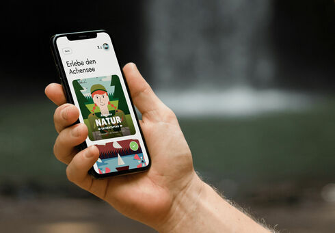Ein Mann hält sein Handy in der Hand und hat die App der Wunderwege mit dem Achensee Naturerlebnispfad geöffnet.