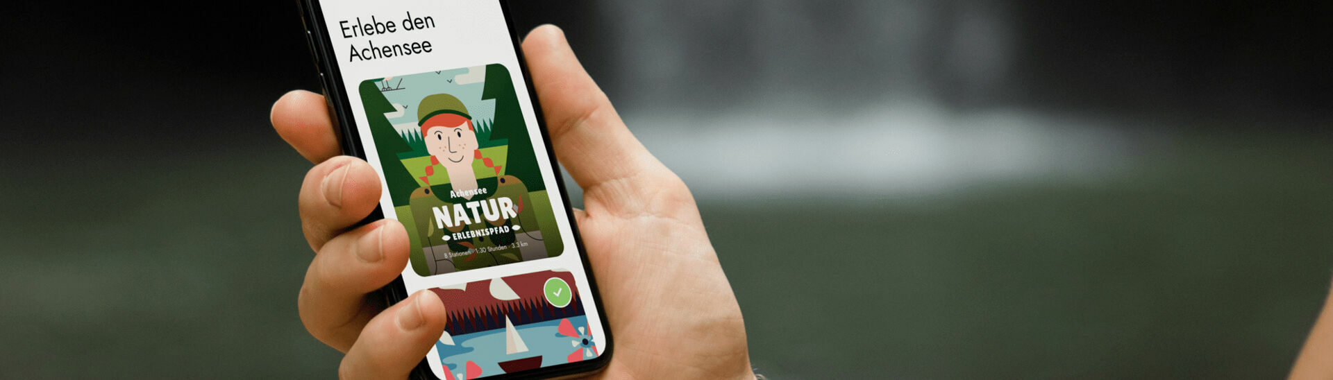 Achensee Natur Erlebnispfad Ein Mann hält sein Handy in der Hand und hat die App der Wunderwege mit dem Achensee Naturerlebnispfad geöffnet.}