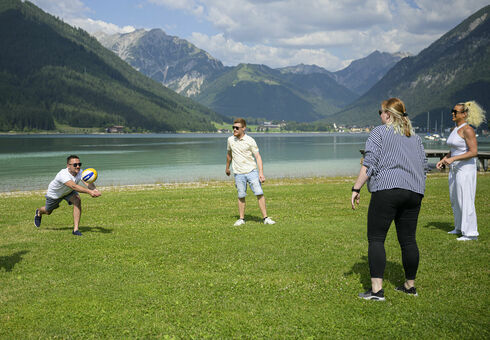 Ein Freundeskreis spielt am Seeufer gemeinsam Volleyball.