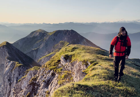 Ein Mann, der auf der Kaserjochspitze vor einem wundervollem gerötetem Himmel geht.