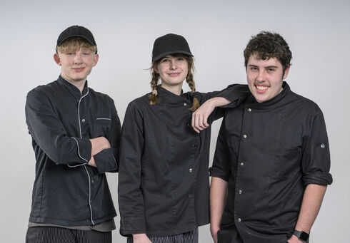 Zwei auszubildende Köche und eine Konditorin posieren vor einer weißen Wand.