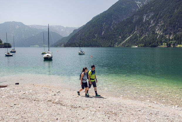 Wandern am Achensee Ein Paar genießt einen kleinen Spaziergang am Ufer des Achensees in Achenkirch. Im Hintergrund sieht man Segelboote.
