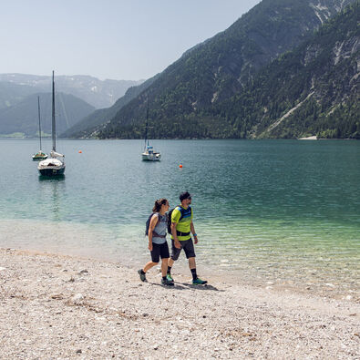A couple enjoying a short walk on the shore of Lake Achensee in Achenkirch. Sailing boats can be seen in the background.
