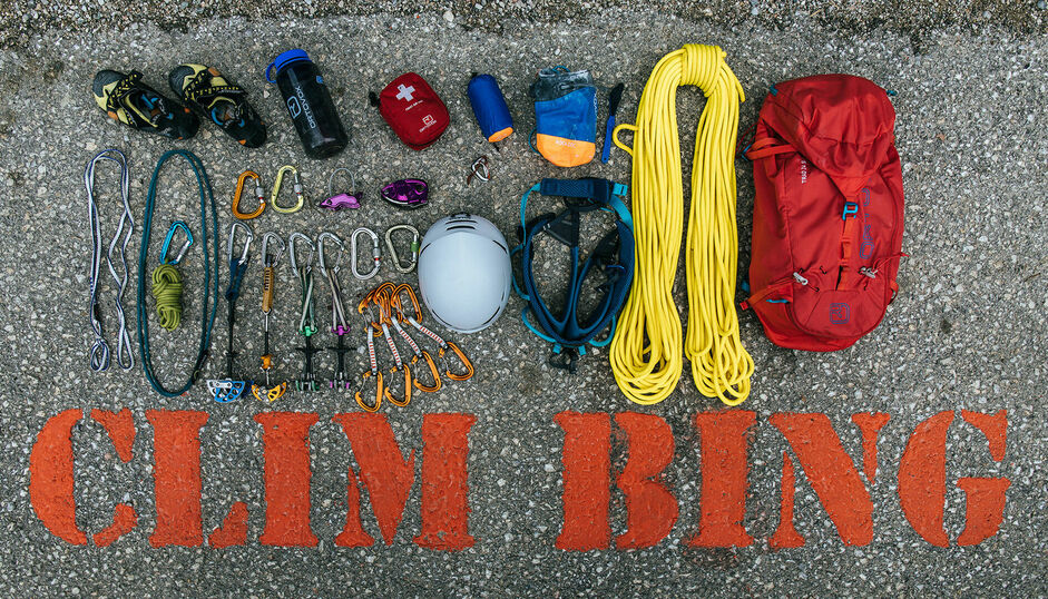 Viel verschiedene Klettercampausrüstung liegt auf dem steinernen Boden (Seil, Karabina, Helm, Rucksack usw.).