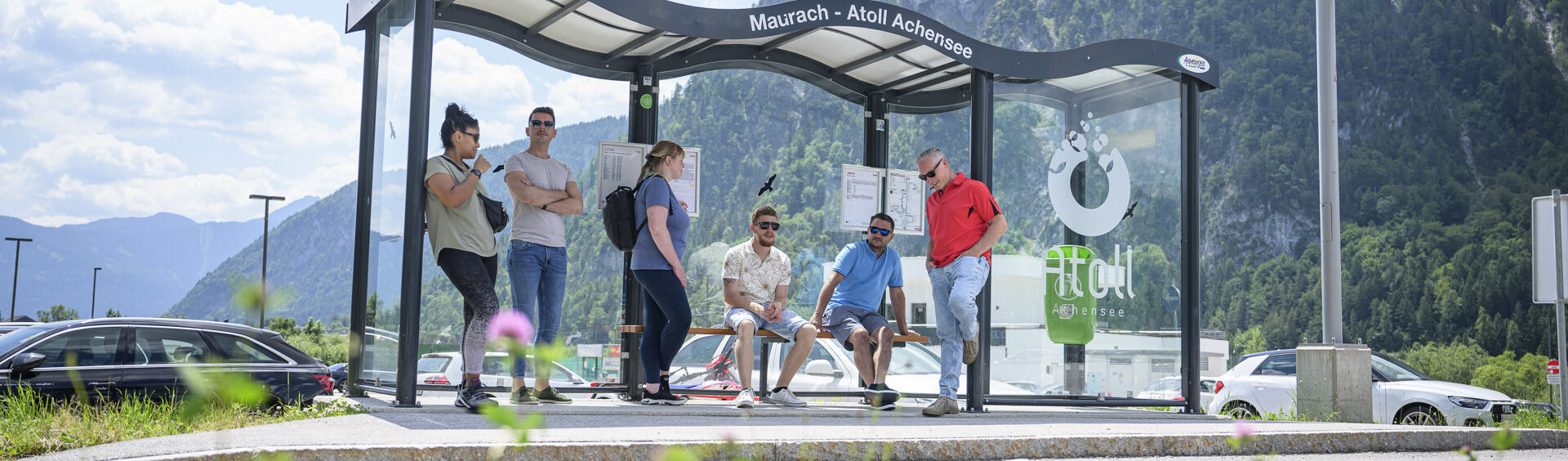 Eine Gruppe Männer und Frauen warten auf den nächsten Bus bei der Haltestelle des Atoll Achensee.