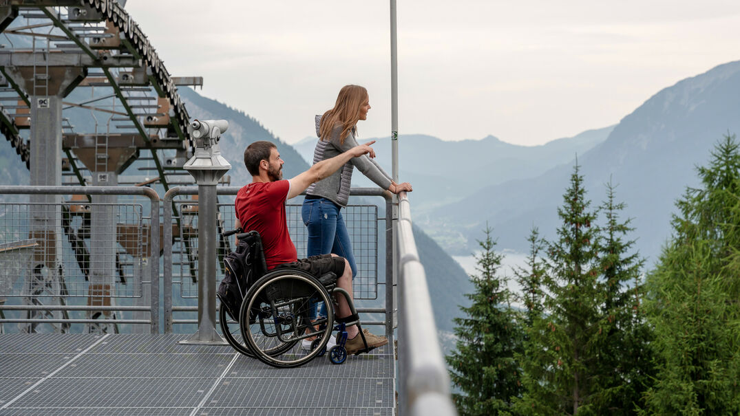 Barrierefreie Karwendel-Bergbahn Ein Mann im Rollstuhl und seine Freundin genießen den Ausblick vom Zwölferkopf auf die Region Achensee im Sommer..