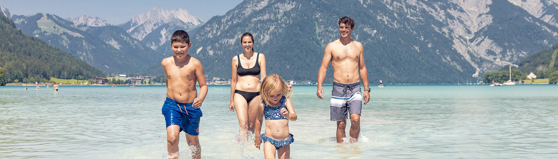 Eine Familie genießt das schöne Wetter und badet im türkisblauen Achensee in Maurach.}