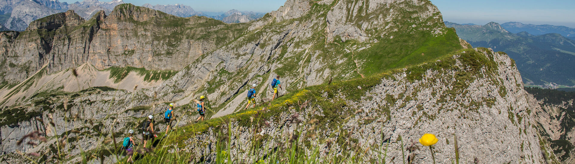 Eine Gruppe Klettersteigcampteilnehmer wandern in Richtung Hochiss bei strahlend blauem Himmel.}