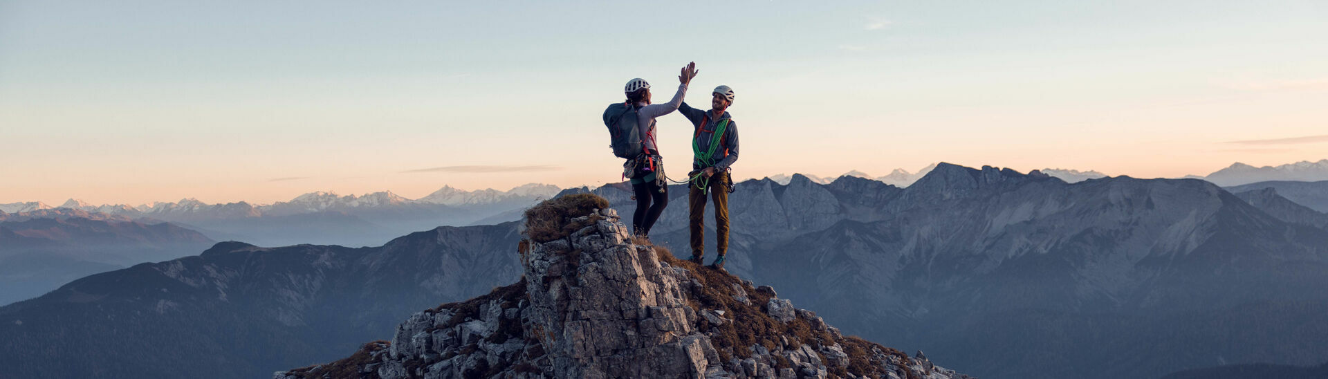 Klettern am Südgrat des Gufferts Zwei Kletterer klatschen miteinander am Gipfel des Gufferts bei leicht gerötetem Himmel ein.}